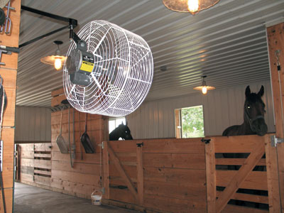 A caged wall fan in a horse barn.